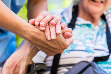 Ältere Person, deren Hand von einem/einer jüngeren PflegerIn gehalten wird