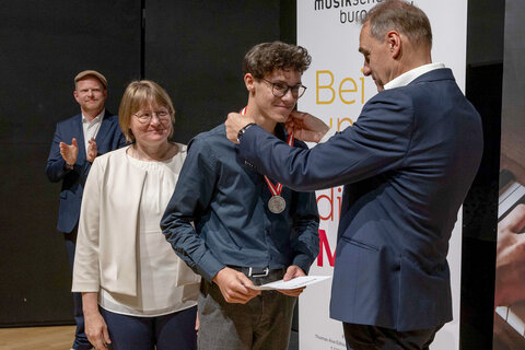 Landesrat Dr. Leonhard Schneemann überreicht prima la musica-Teilnehmer Benjamin Pucher (Instrument: Hackbrett) eine Silbermedaille.