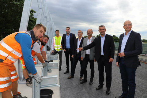 Infrastrukturlandesrat Heinrich Dorner (l.) und Großhöfleins Bürgermeister Heinz Heidenreich (r.) lassen sich von Christopher Sifkovits (Fa. Granit) die Vorzüge des neuen Flüsterasphaltes erklären.