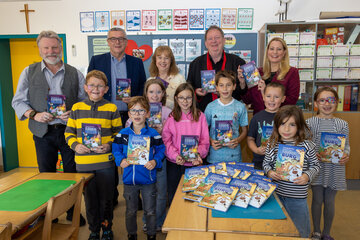 Direktor Karl Hofwimmer (VS Breitenbrunn), Bürgermeister Helmut Hareter, Schulqualitätsmanagerin Michaela Seidl (Bildungsdirektion Burgenland), Horst Horvath (Verlagsleitung, edition lex liszt 12) und Landesrätin Daniela Winkler (hinten v.l.) mit Kindern der Volksschule Breitenbrunn bei der Übergabe der Bücher „Die fliegende Burg“ von Thomas Brezina.