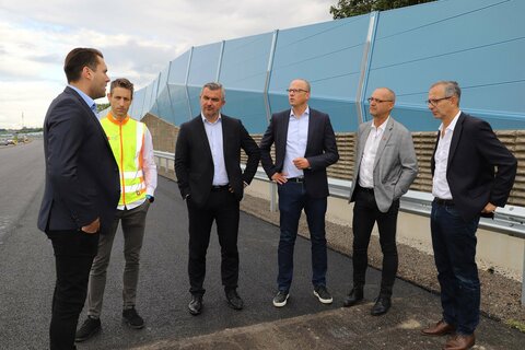 Roland Beisteiner von tz baumanagement, Christopher Sifkovits von der Firma Granit, ASFINAG Baumanagement-Geschäftsführer Alexander Walcher, Großhöfleins Bürgermeister Heinz Heidenreich, Infrastrukturlandesrat Heinrich Dorner und ASFINAG Baumanagement-Geschäftsführer Andreas Fromm mit Arbeitern auf der Baustelle.
