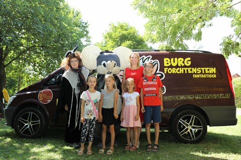 Landesrätin Mag.a (FH) Daniela Winkler (hinten r), Burgmaus Forfel (hinten Mitte), Gruselhexe Griselda (hinten l) und Kinder vor dem Tourbus von Burg Forchtenstein Fantastisch;