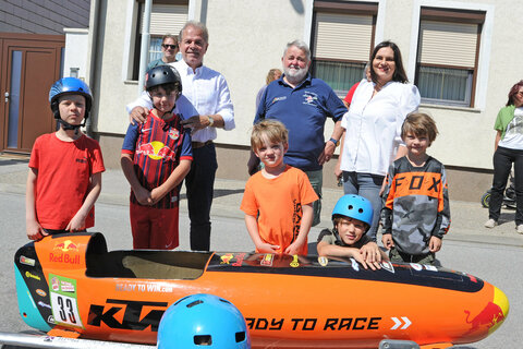 Landeshauptmann-Stellvertreterin Mag.a Astrid Eisenkopf (hinten, rechts) mit Bürgermeister Ing. Harald Neumayer sowie Obmann Wilhelm Absenger (hinten, v.l.) mit Teilnehmer*innen vor dem Start des Seifenkistenrennens in Purbach.