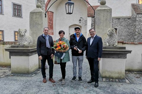 Burghotel-Direktor Marc Six (l.) und Burg- und Ausstellungskoordinator Norbert Darabos (r.) überreichten Sabine Hutter als 100.000-ste Besucherin einen Blumenstrauß und ihrem Bruder Dominik ein Geschenk.