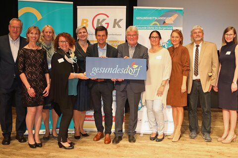 Landesrat Christian Illedits (Mitte), BGKK-Obmann Hartwig Roth (5.v.r.) und BGKK-Direktor Christian Moder (2.v.r.) sowie Dr. Karl Mach (l.) und Mitarbeiterinnen sowie der "Gesundes Dorf"-Tafel im Kulturzentrum Oberschützen.