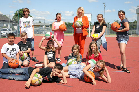 Bildungslandesrätin Mag.a (FH) Daniela Winkler präsentierte mit MS Direktorin LAbg. Rita Stenger, BEd, und Bürgermeister Mag. Rainer Porics die Details zur Ferienbetreuung (im Bild nach PK gemeinsam mit Kinder am Hartplatz der Schule)