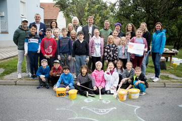 Landesrat Mag. Heinrich Dorner (2.v.l., stehend) und Mag. Tina Wurm (rechts stehend) von der Mobilitätszentrale sowie Volksschuldirektorin Dipl. Päd. Elisabeth Seifried, MA sowie Lehrerinnen und Lehrern und Schülerinnen und Schülern der Volksschule Oberpullendorf beim Bemalen der Straße.