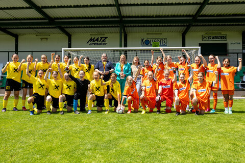 Franz Schneider (Stadtrat Neusiedl), Landesrätin Daniela Winkler und Kerstin Bayer (Landesreferentin Mädchenschülerliga) mit den Finalmannschaften Gymnasium Kurzwiese Eisenstadt (gelbe Trikots) und Gymnasium Oberpullendorf (orange Trikots).