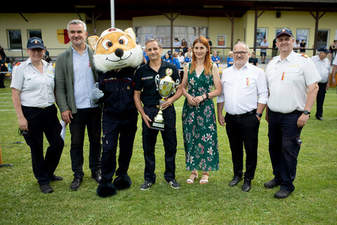 OBI Thomas Buzanich (4.v.l.), Kommandant der Freiwilligen Feuerwehr Kroatisch Minihof, erhielt von Landesrat Heinrich Dorner, Landtagsabgeordnete Carina Laschober-Luef, Bürgermeister Christian Balogh, Landesfeuerwehrkommandant-Stellvertreter LBDS Martin Reidl und Bezirksfeuerwehrjugendreferentin HBI Barbara Wessely einen Pokal als Dank und Anerkennung für die Austragung des Bewerbes.