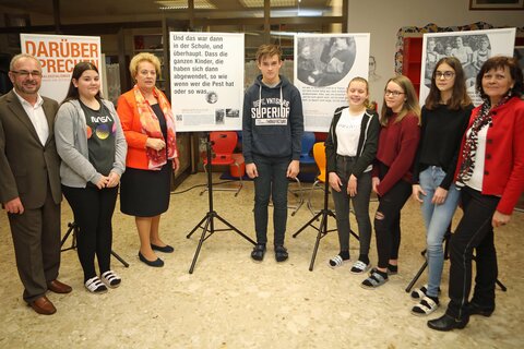 Direktor Gerd Kirschner, BEd.MSc (l.), Landtagspräsidentin Verena Dunst (3.v.l.) und Lehrerin Renate Fandl (r.) mit Schülerinnen und Schülern vor den Tafeln der Ausstellung in der Mittelschule.