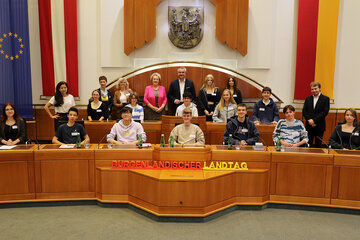 Landesrat Mag. Heinrich Dorner und Landtagspräsidentin Verena Dunst (hinten, Mitte) begrüßten gemeinsam mit DDr. Barbara Glück und (l., stehend) und Jonathan Dorner (r., stehend) die Schülerinnen und Schülern des BG/BRG Mattersburg im Landtagssitzungssaal.