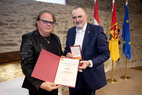 Landeshauptmann Hans Peter Doskozil überreichte die Urkunde und das Komturkreuz an Musiker, Produzent und Gitarrist der Band Opus, Ewald Pfleger.