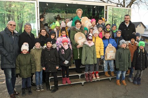 Schulqualitätsmanager Erich Deutsch, Bürgermeister Vinzenz Knor, Landtagspräsidentin Verena Dunst, Direktorin Sabine Unger, Dr. Charlotte Clement und Landesrat Heinrich Dorner mit den Schülerinnen und Schülern der Volksschule vor der mobilen jagdpädagogischen Einrichtung.